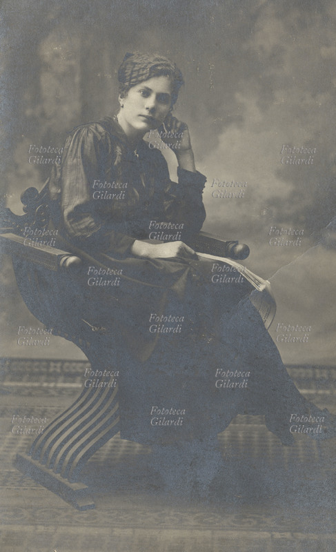 Donna, fine 1800. Elegante signora ritratta fotograficamente seduta con in mano un giornale, simbolo di emancipazione.