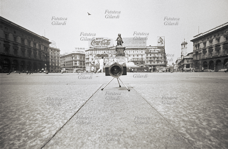 STORIA DELLA FOTOGRAFIA veduta di piazza del Duomo a Milano semivuota, con la macchina fotografica Hologon installata su treppiede per la ripresa rasoterra dei piccioni che beccano il mangime lanciato dai turisti. L\