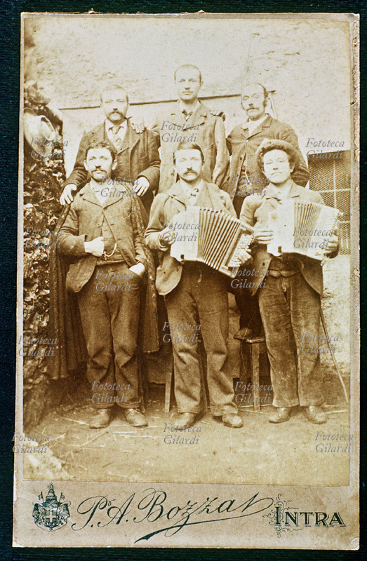 MUSICA Gruppo di cinque amici posano per una fotografia ricordo. In primo piano due di loro suonano la fisarmonica a bottoni. Fotografia P.A. Bozza, Intra 1899 circa.