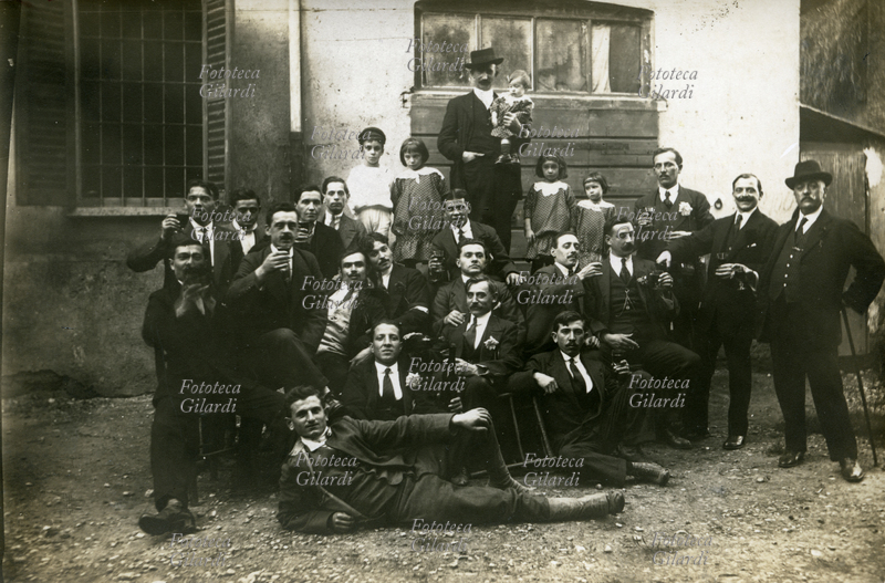 MILAN 1915 Group mainly composed of adult men (with the exception of five children gathered around the central figure, holding the smallest one) immortalized by the photographer in a joyful toast. Souvenir photography: "Group made at the restaurant of the Gambero in Lambrate after a breakfast offered by the Motoristi team to the Bianchi chief. 7-11-1915"