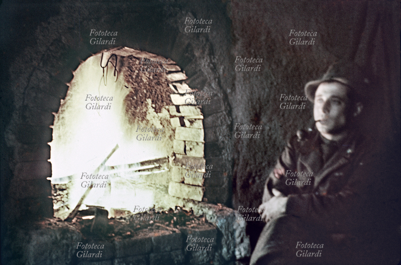 SECONDA GUERRA MONDIALE Zona di Babka (ansa del Don), caporalmaggiore Nicolis, alpino che morirà un mese dopo durante la ritirata, si riposa al fuoco di un forno sotterraneo costruito per rendere più sopportabile la vita di prima linea. Fotografia eseguita dal tenente Roberto Cacchi, autore di numerose preziose testimonianze fotografiche a colori della tragica spedizione in Russia, reduce sopravvissuto della 2^ Divisione alpina "Tridentina", 6° Reggimento Alpini al comando del colonnello Paolo Signorini, Battaglione Verona. URSS inverno 1942