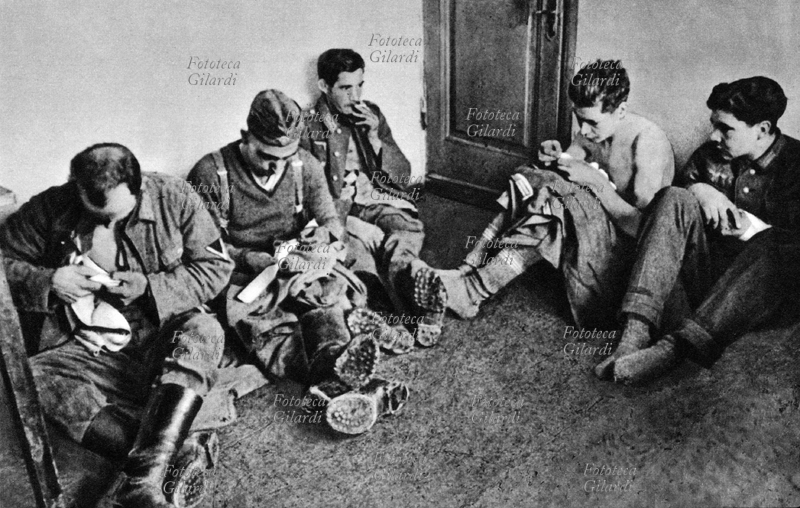 WWII German soldiers in a Soviet prison camp, sitting on the ground, are intent to comb and trim their clothing. USSR 1945