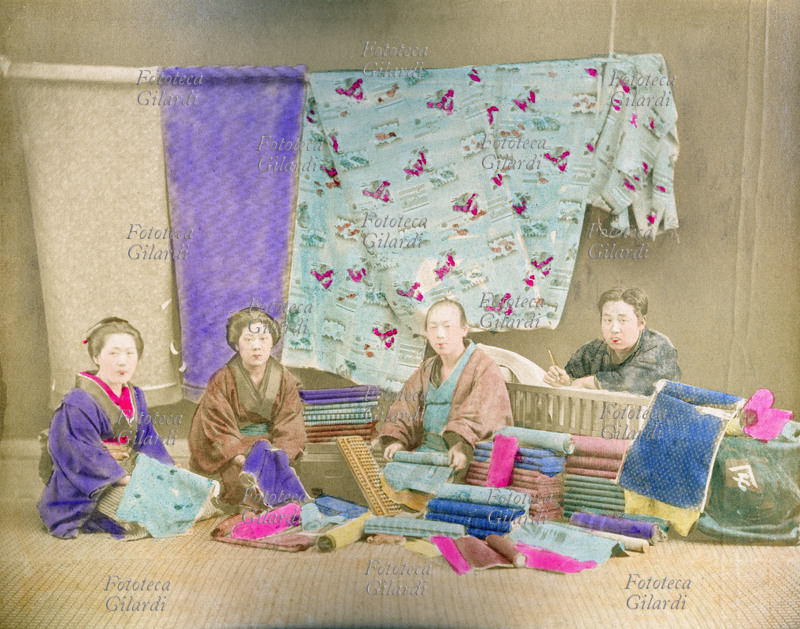 GIAPPONE 1890 Quattro venditori di stoffe, ritratti seduti tra la loro mercanzia, periodo Meiji (1868-1912). Fotografia colorata manualmente, 1890.
