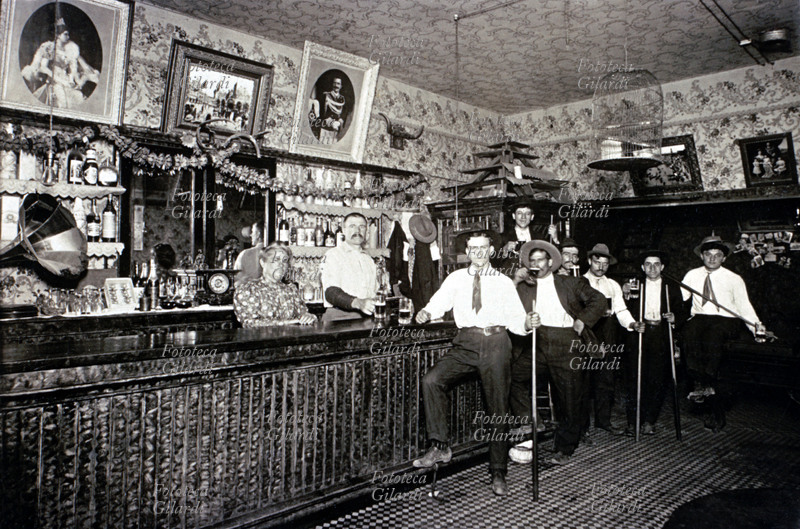 EMIGRAZIONE Un bar gestito da emigrati piemontesi in Arizona. Fotografia ricordo in posa accanto al bancone, 1905. Da notare i ritratti dei reali italiani appesi sopra al banco. Uno dei clienti (ragazzo in primo piano) viene da Cosio (Sondrio, Lombardia) nel 1891, all\