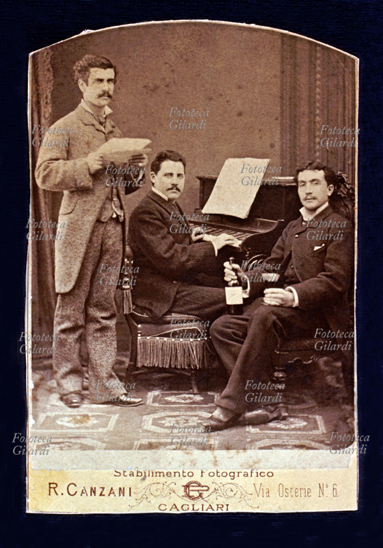 VINO Fotografia ricordo: un pianista un cantante ed un intenditore (di musica e di vino) posano per il fotografo. Cagliari, stabilimento fotografico R. Canzani, primi anni del XX secolo