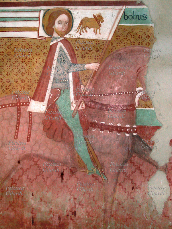 SAN BOVO (940 circa – 22 maggio 986) nobile cavaliere provenzale dedito alla penitenza e ai pellegrinaggi rappresentato a cavallo con lo stendardo che raffigura i buoi, simbolo dello spirito di sacrificio, della virtù del lavoro e della sottomissione alla Parola di Dio. Dettaglio dagli affreschi attribuiti alla scuola di Manfredino e Franceschino Boxilio sulla colonna centrale nell\