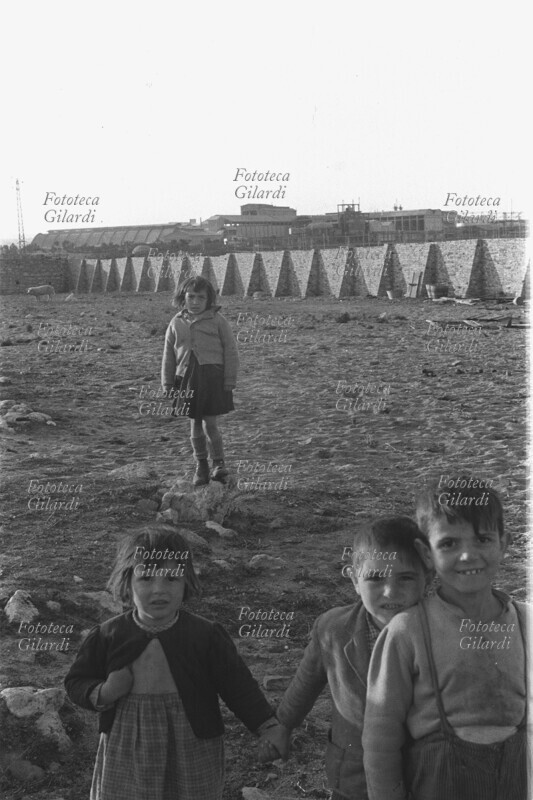 INDUSTRIALIZZAZIONE bambini di circa cinque-sei anni giocano a rimpiattino nei pressi delle mura della Montecatini, nella zona dove si allevano maiali e galline; i tre in primo piano sorridono dinanzi all\