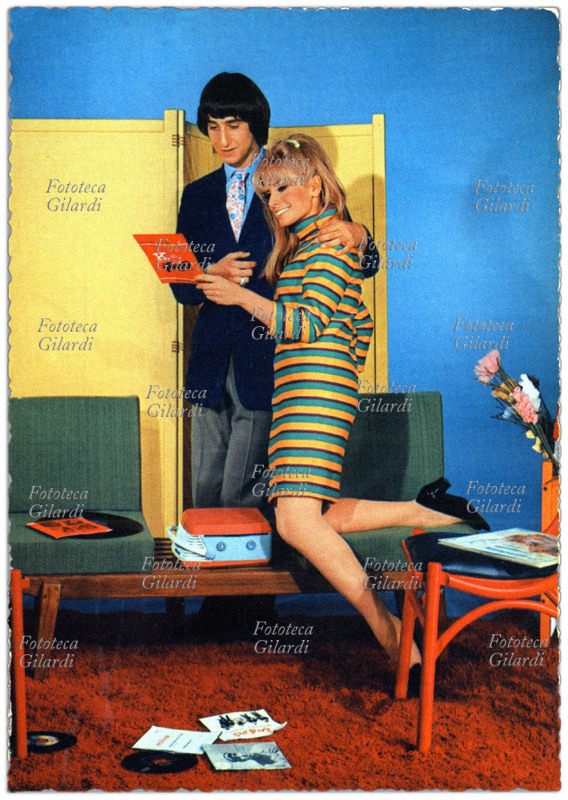 ITALY, 1960s. An embracing couple admires the 45 rpm record of their latest hit before playing it on the record player. Beat fashion arrives in Italy too. Postcard, Italy, circa 1965.