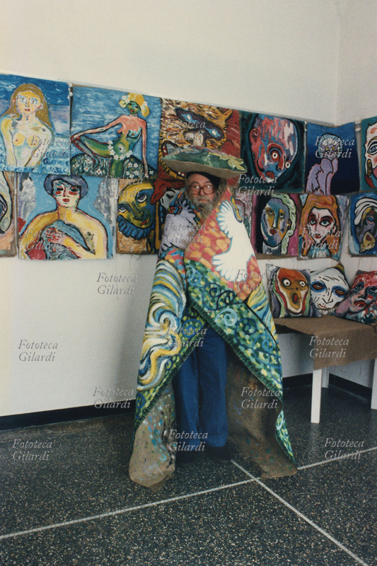 Ando GILARDI ha voluto farsi ritrarre così: avvolto in un tappeto dipinto e sullo sfondo delle sue opere-cuscino esposte nella mostra: \