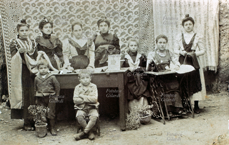 MESTIERI Fotografia di gruppo in una piccola sartoria artigianale: sette donne (alcune molto giovani) tra le quali la seconda da sin. probabilmente era la proprietaria. Davanti al tavolo dei tagli due bambini: seguivano le mamme sul posto di lavoro. Sulla destra l\
