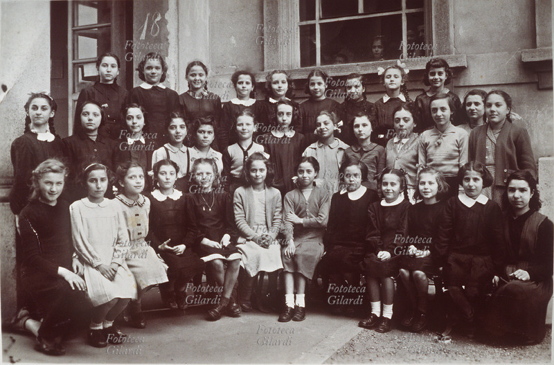 SCUOLA Insegnanti ed allieve di una classe elementare della fine degli anni Quaranta posano per una foto di gruppo nel cortile della scuola. Da una finestra, alcune allieve di un\