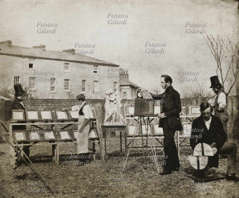 William Henry Fox TALBOT (1800-1877) Il suo laboratorio fotografico. A sinistra, due file di telai esposti alla luce del sole per la stampa a contatto delle copie fotografiche, a destra un momento di ripresa con macchina su cavalletto. Gran Bretagna, 1840 circa