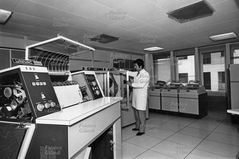 SETTORE TERZIARIO Sala di custodia delle memorie magnetiche della Banca Alto Milanese, un tecnico apre lo sportello di accesso alle bobine. In primo piano una gigantesca stampante. Fotografia di Ando Gilardi (1921 - 2012) #andogilardi, Busto Arsizio, 1970 circa.