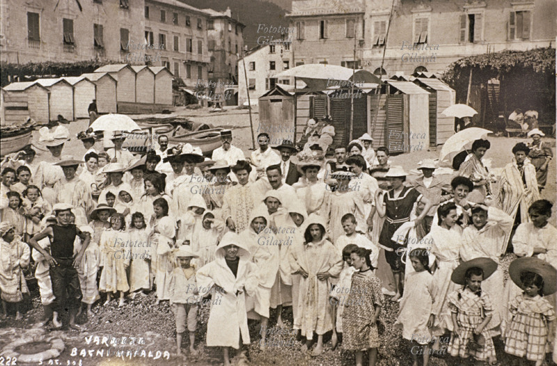 MARE sulla piccola spiaggia ai Bagni Mafalda di Varazze (SV) gruppo festoso e disordinato di bagnanti in accappatoio bianco, nella maggior parte bambini e donne. Fotografia viraggio seppia, Varazze 1908