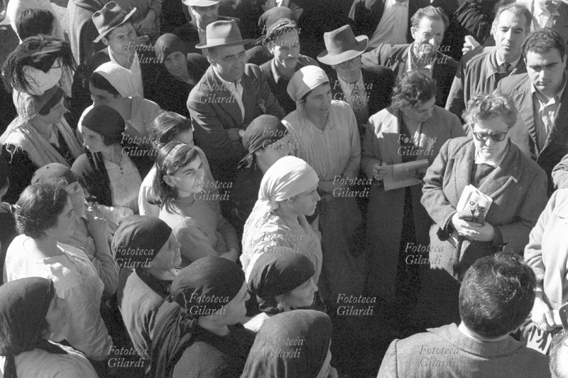 SINDACALISMO Incontro dei membri della commissione di inchiesta del sindacato e dei braccianti. A destra Anna De Lauro Matera (1909 – 2003). È un giorno festivo: gli abitanti della cittadina seguono il comizio in piazza. La ripresa dall\
