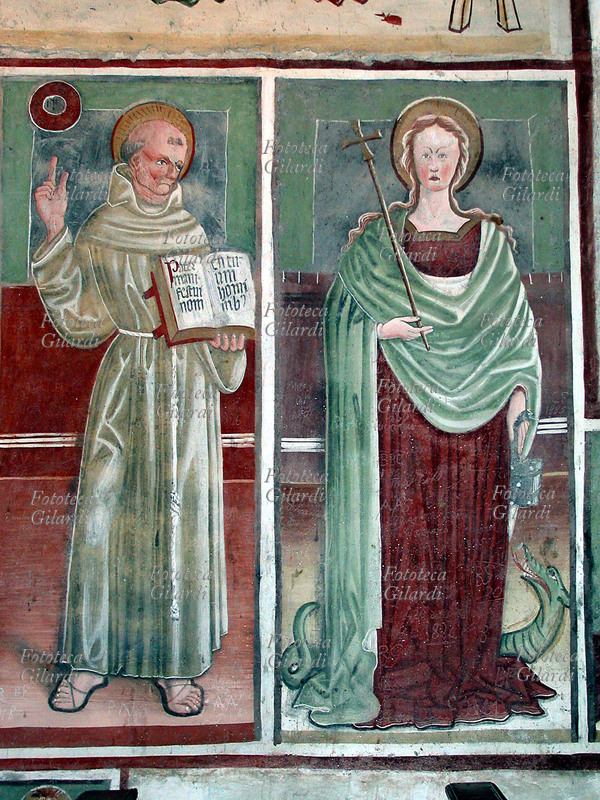 SANTI San Bernardino da Siena (8 settembre 1380 – 20 maggio 1444), francescano, teologo e predicatore italiano, e Santa Margherita di Antiochia martire (275 – 290) con la Croce, che schiaccia il drago sotto i piedi. Affresco di Antonio Baschenis, Carisolo (Trento), XV secolo.