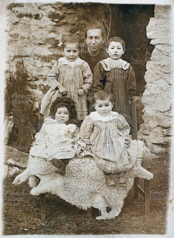 FAMIGLIA nonna in posa con quattro nipotine, in esterno sullo sfondo di una casa in pietra e appoggiate sopra una pelliccia bianca; la più piccola indossa un\