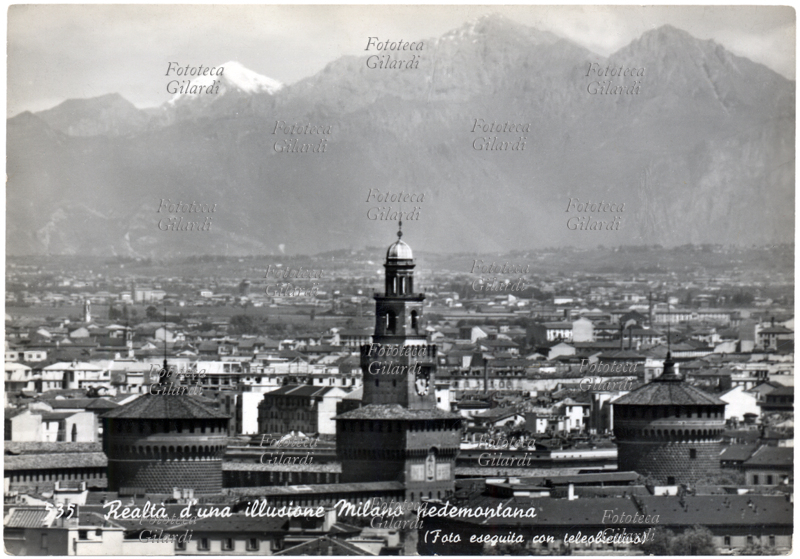 MILANO - Realtà di una illusione, Milano pedemontana. Nella foto eseguita con teleobiettivo le Alpi sembrano innalzarsi alle porte della metropoli lombarda. Cartolina postale, fotografia circa 1953.