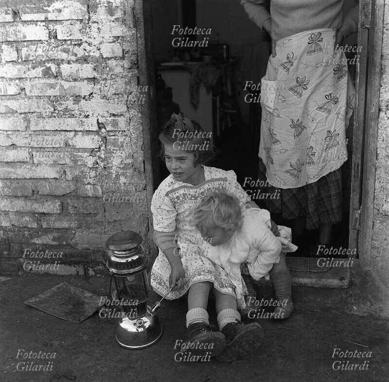 BAMBINE giocano con una lampada a gas, sedute sulla soglia di casa, sorvegliate dalla madre. Fotografia di Ando Gilardi (1921-2012) #andogilardi, Borghetto dell\