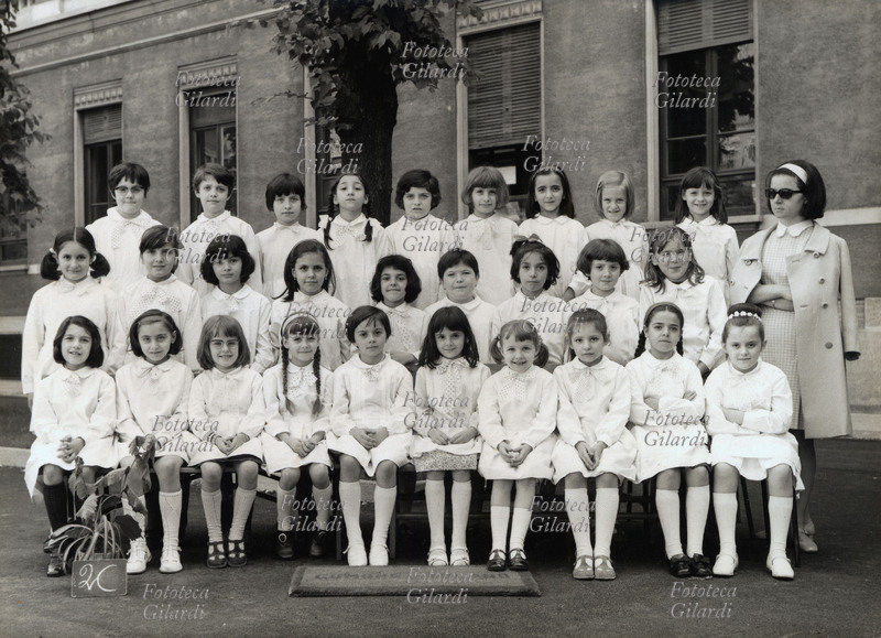 SCHOOL Photography memory of a feminine class of the elementary ones, 2C. The pupils wear all the classic white apron, the master puts down to the side of the group with the dark glasses and a severe expression. Italy, 1968.