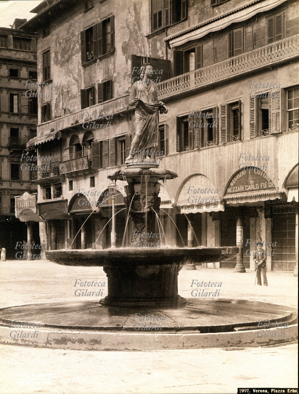 VERONA Piazza delle Erbe: la fontana di Madonna Verona (fatta erigere nel 1368 da Cansignorio) che presenta vasca e stelo ornati da teste in rilievo e figure simboliche (opera forse di Bonino da Campione) ed è sormontata dalla figura di Madonna Verona, statua romana del I sec. d.C., le cui parti mancanti di testa e braccia furono fatte completare da Cansignorio al momento della realizzazione della fontana. Fotografia, fine XIX secolo