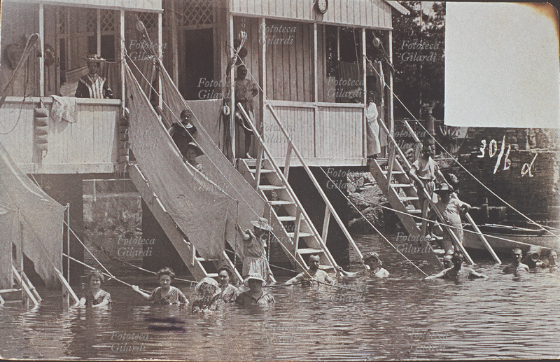 VACANZE Uno dei primi stabilimenti balneari talassoterapici, munito di cabine e comode scalette per un accesso diretto al mare. La struttura è dotata di personale, messo a disposizione dei bagnanti per le immersioni curative. In acqua si possono notare anche delle corde, appositamente tese per sostenersi durante bagni prolungati. Italia, 1880.