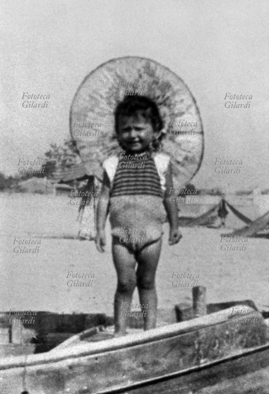 Raffaella CARRÀ (18 June 1943 - 5 July 2021) stage name of Raffaella Pelloni, portrayed here at the age of 2 on the beach of Bellaria-Igea Marina (Rimini), the town where she spent her early childhood. After her debut as a child actress and some participations in national and foreign films, the real success with which she achieved international fame came not from her career as an actress, but for her skills as a showgirl, singer, dancer, actress, TV presenter and author. . Photograph, Italy 1945