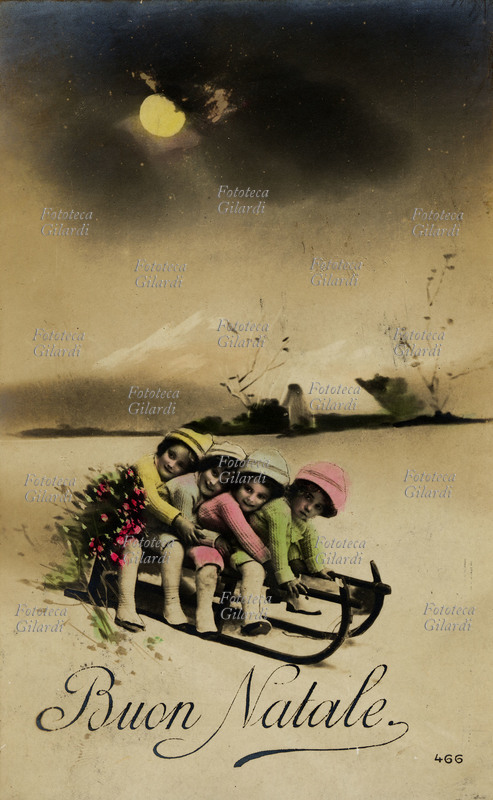 BUON NATALE quattro bambine lo augurano scivolando sulla neve tutte con un unico slittino. Cartolina augurale fotografica colorata manualmente, Italia 1916.