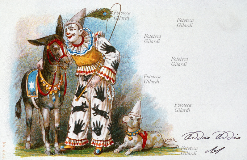CIRCO clown bianco recita il suo numero comico con un asinello ed un cane di media taglia, entrambi in costume di scena. Sta sussurrando qualcosa nell\