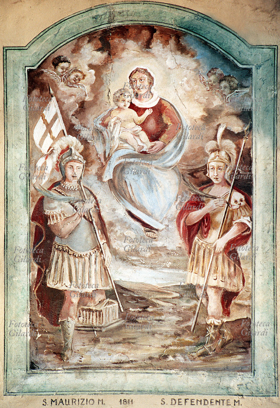 San MAURIZIO (? – 287 circa) e San DEFENDENTE (? - 287 circa) martiri; il primo, generale capo della Legione Tebea, il secondo semplice legionario al suo comando. Entrambi vittime delle decimazioni inflitte alla legione per essersi rifiutata di obbedire agli ordini di massacrare i cristiani del Vallese. Fra i due martiri, la Vergine in Gloria con il Bambinello e angeli. Affresco, Sampeyre (Cuneo), frazione Calchesio, 1811. Fotografia di Elena Piccini, Italia 2002.