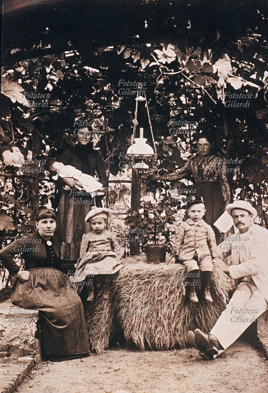 FAMIGLIA gruppo familiare composto dei due genitori, in primo piano, con figli maschio e femmina e in attesa del terzo, e in secondo piano da due giovani donne, (forse sorelle) delle quali una, l\