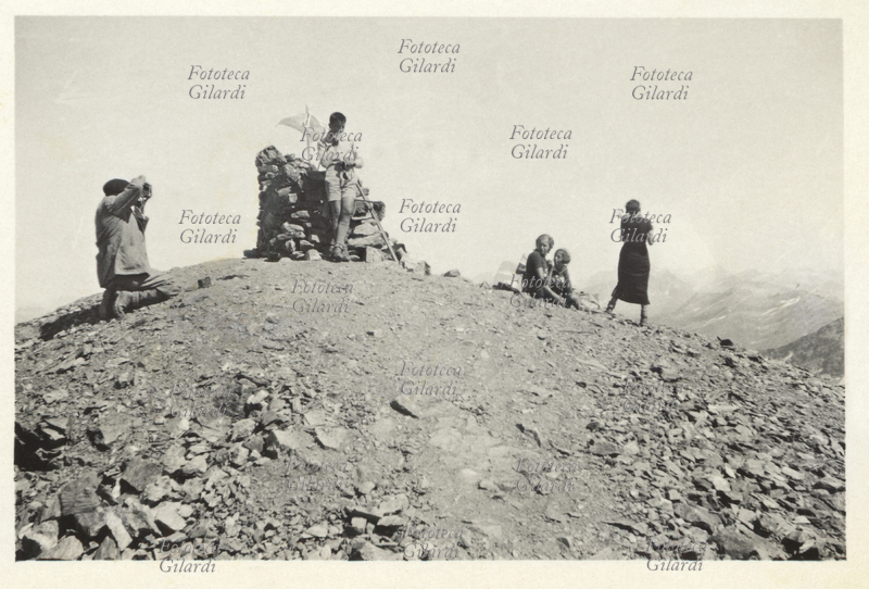 TURISMO in montagna, famiglia in passeggiata estiva sulle prealpi del comasco. Sul colmo di un rilievo, mentre parte del gruppo ammira il panorama altri riprendono la scena con la macchina fotografica. Italia, zona del comasco, 1925 circa.