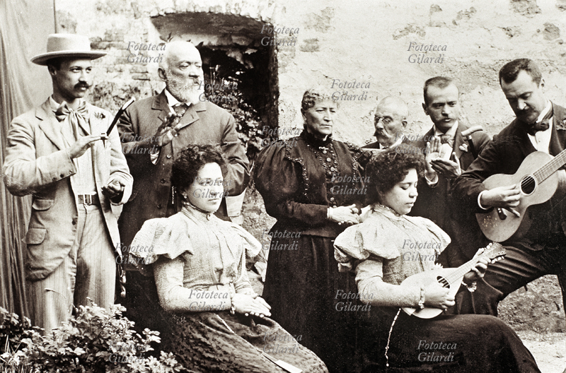 MUSICA Gruppo di musicisti in una fotografia della fine del XIX secolo. Una elegante donna suona il mandolino accompagnata dalla chitarra; gli altri componenti, sguardo al direttore, scandiscono il tempo con il battito delle mani. Fotografia, Italia circa 1890