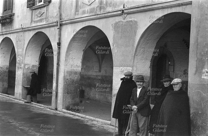 ITALIA Venosa, veduta dei portici con gli anziani del paese. Fotografia di Ando Gilardi (1921-2012) #andogilardi, parte di un ampio servizio realizzato per \