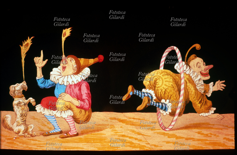 CIRCO Un clown ed il suo cane tengono una piuma di pavone in equilibrio sul naso, mentre un altro clown salta nel cerchio. Vetrofania per lanterna magica, XIX secolo.