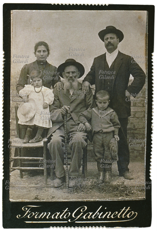 FAMIGLIA Genitori con due nipoti posano accanto al nonno seduto al centro. Il vecchio ha una bellissima barba bianca bipartita, i figli gli appoggiano una mano sulle spalle. Fotografia \