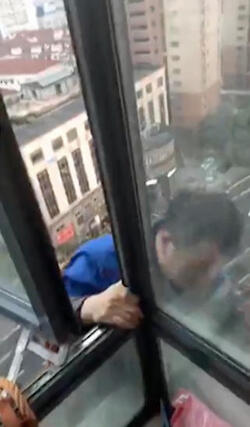 PIC BY SHANGHAI OBSERVED / CATERS NEWS - (PICTURED: The repairman then makes his way off the window and down towards the air con unit.) - Talk about having to keep your cool, this is the bizarre moment a daredevil repairman uses his customer as a counterweight to dangle out of an eleventh storey window and fix his air con. Having checked the length of his harness, the maintenance man leaps on to the precariously skinny window ledge of the apartment in Old Town Shanghai, China, to check his best route. After wrapping the bright orange rope around the American ex-apt who runs Shanghai Observed, the resourceful fixer then ties one end of the binds to a curtain rail. Finally clambering out of the tight window, the repairman lowers out of sight of the ledge while we are treated to just how dizzyingly high up the flat is with views of the traffic and pedestrians looking tiny below. - SEE CATERS COPY