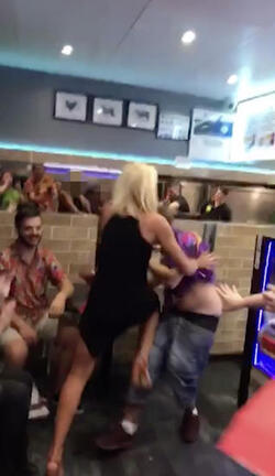 PIC FROM MERCURY PRESS (PICTURED: THE WOMAN ATTEMPTS TO LAND A KNEE TO THE RIBS OF LEWIS CALEY IN A TAKE AWAY IN CLACTON-ON-SEA IN ESSEX) This is the moment a foul-mouthed blonde lady launched herself at a drunken reveller in a shocking takeaway brawl - because he suggested she was in her 60s and threw a chip in her face. Lewis Caley and his friends were getting food from the Quality Diner takeaway in Clacton-on-Sea, Essex, after celebrating his 20th birthday. However an argument ensued when cocky Lewis asked one of the women - estimated to be in her 30s - how old she was and then jokingly suggested she was in her 60s. Footage shows the blonde brand jolly engineer Lewis a c**t and then repeatedly try to snatch his food from him as he sits eating. SEE MERCURY COPY