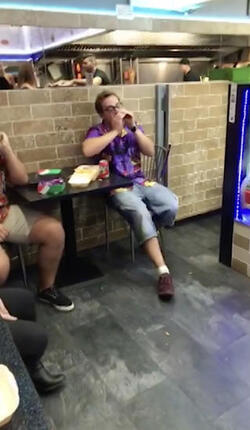 PIC FROM MERCURY PRESS (PICTURED: LEWIS CALEY ATTEMPTING TO SHARE A JOKE WITH THE BLONDE WOMAN IN A TAKE AWAY IN CLACTON-ON-SEA IN ESSEX) This is the moment a foul-mouthed blonde lady launched herself at a drunken reveller in a shocking takeaway brawl - because he suggested she was in her 60s and threw a chip in her face. Lewis Caley and his friends were getting food from the Quality Diner takeaway in Clacton-on-Sea, Essex, after celebrating his 20th birthday. However an argument ensued when cocky Lewis asked one of the women - estimated to be in her 30s - how old she was and then jokingly suggested she was in her 60s. Footage shows the blonde brand jolly engineer Lewis a c**t and then repeatedly try to snatch his food from him as he sits eating. SEE MERCURY COPY